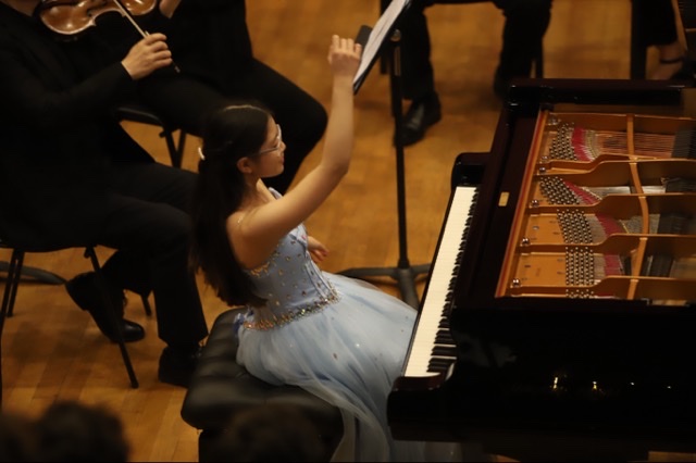 A pianist at the keyboard, arm raised towards the orchestra